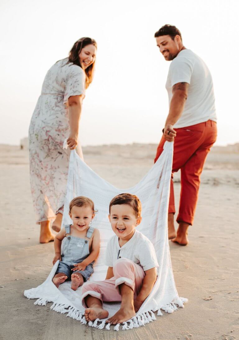 kids on a blanket and parents pulling on the beach for family pics